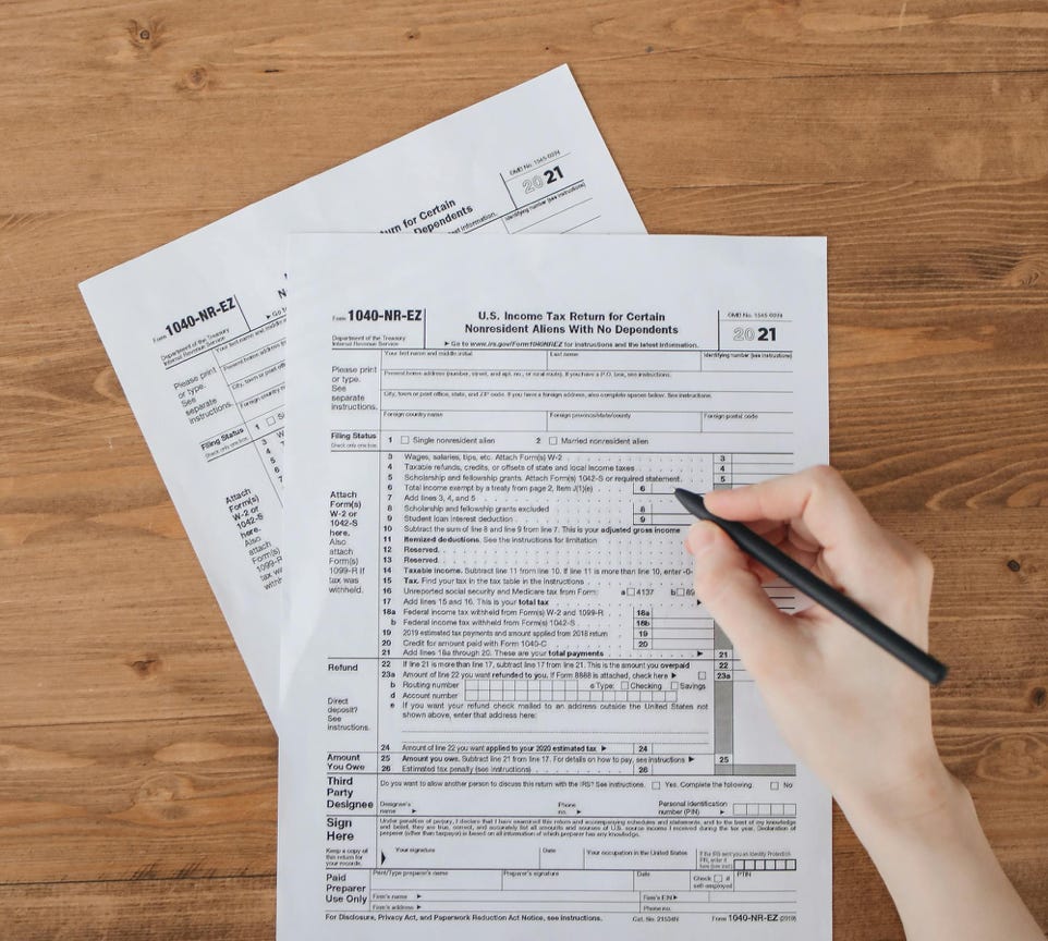 A Person Filling Out Taxation Documents on a Wooden Flat Surface